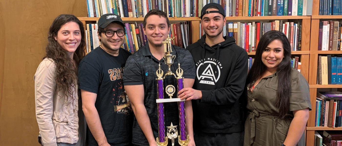四名“道德碗”优胜者在书架前举着一个大奖杯.